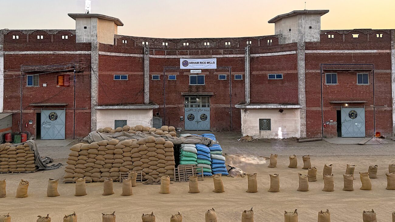 Front view of Arham Rice Mills factory with stacked rice bags outside.