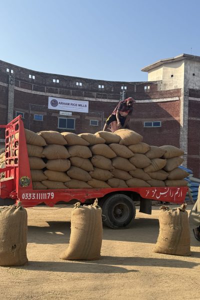 Worker stacking filled rice bags on red transport trolley at Arham Rice Mills processing yard.